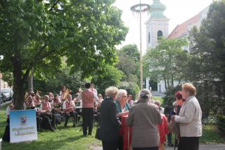 Im Vordergrund die Besucher, im Hintergrund der Musikverein, die Pfarrkirche Leopoldau und der Maibaum.
